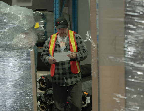 Warehouse worker examines paperwork amidst stacks of pallets and shelving units